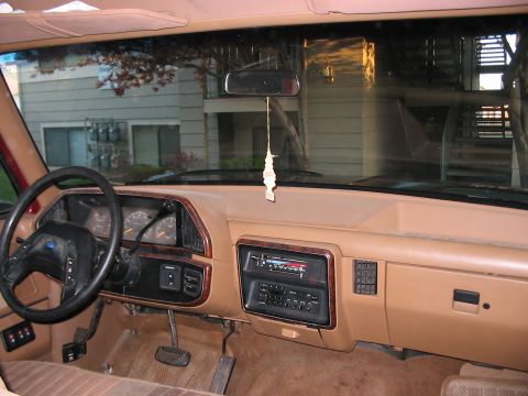 1991 Ford Bronco - The interior of a truck shows the dashboard, steering wheel, and radio, with a view of an apartment building through the windshield.