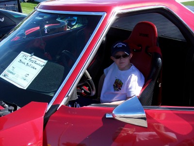 1972 Ford Ranchero - A young boy sits in the driver's seat of a red 1972 Ford Ranchero, which has a sign on the windshield.