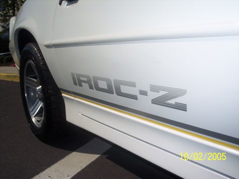 1988 Chevrolet Camaro - The side of a white vehicle displays an IROC-Z decal and a thin yellow accent stripe.