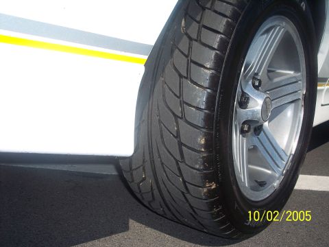 1988 Chevrolet Camaro - Close-up of a car's wheel and tire, showing a yellow stripe on the white bodywork.