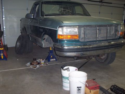 1996 Ford Bronco - A green Ford truck is raised on jack stands in a garage, with its front tires removed for maintenance.