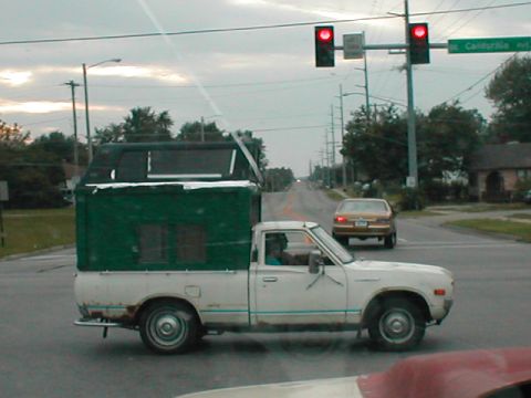 1979 Ford Bronco - A white pickup truck with a custom green camper shell drives down the road.