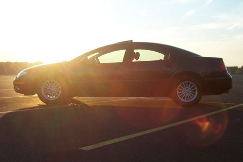 1999 Chrysler 300M - A black sedan is parked in a lot with the sun setting behind it, creating lens flare.