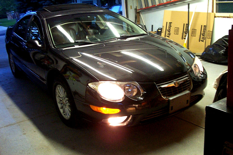 Black Chrysler 300M sedan in a garage at night with headlights on, front three-quarter view