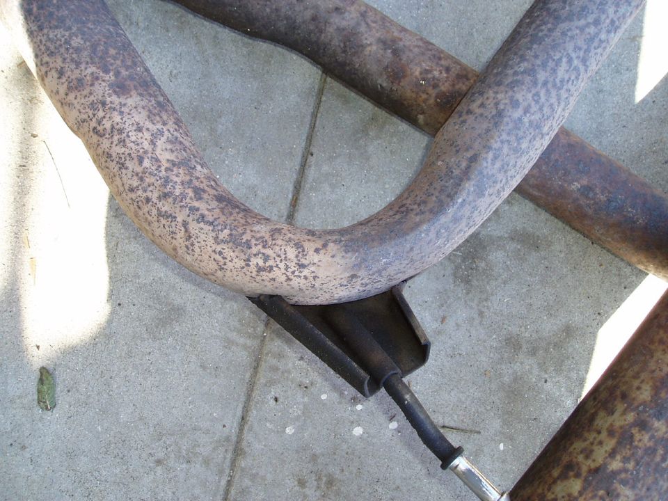 Rusty exhaust pipes with a metal bracket and cable, resting on a concrete surface
