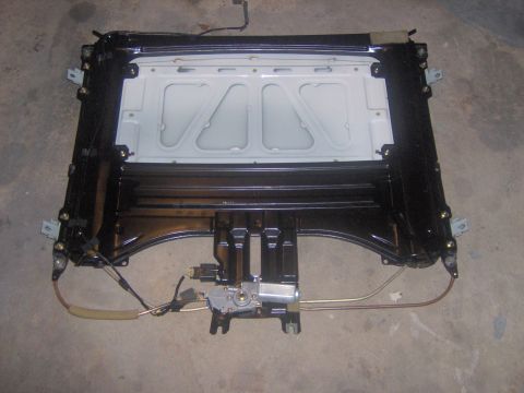 1994 Ford Probe - A complete sunroof assembly unit removed from a vehicle, showing the black metal frame, white painted panel, wiring, cables, and the drive…