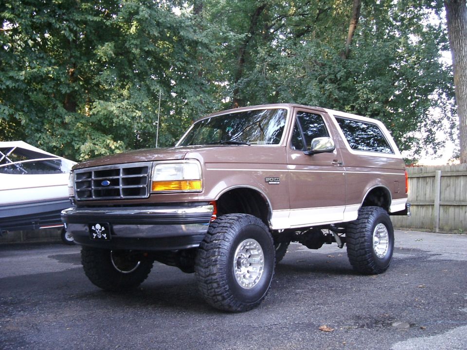 Lifted brown Ford Bronco on mud tires, 3/4 front view in driveway