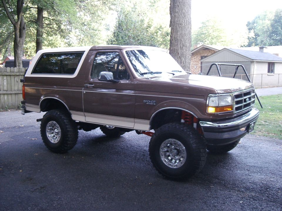 Lifted brown and tan Ford Bronco with white hardtop and mud tires on driveway