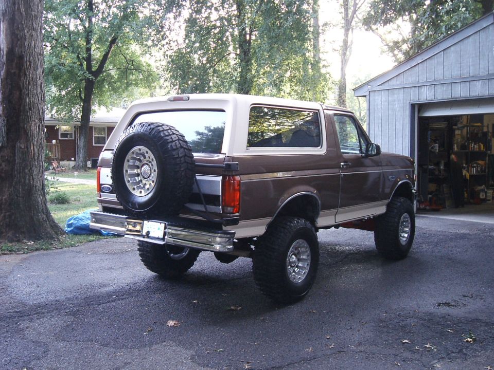 Lifted two-tone brown and tan Ford Bronco with rear-mounted Swamper spare tire, seen from the rear quarter