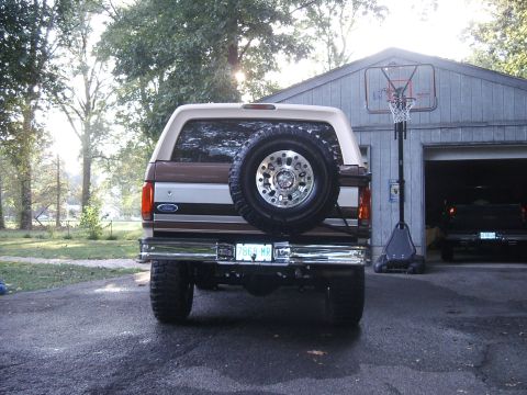 1993 Ford Bronco - This lifted 1993 Ford Bronco features a rear-mounted spare tire and custom wheels, parked in a driveway.