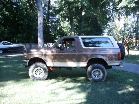 1993 Ford Bronco - Side view of a lifted 1993 Ford Bronco parked outdoors on a grassy area.