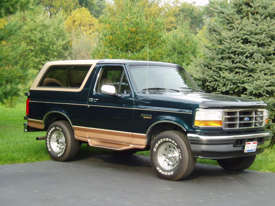 Dark green and tan Ford Bronco parked on a driveway in front of evergreen trees