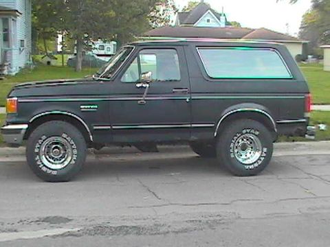 1989 Ford Bronco - Side profile of a dark-colored 1989 Ford Bronco parked on a residential street.