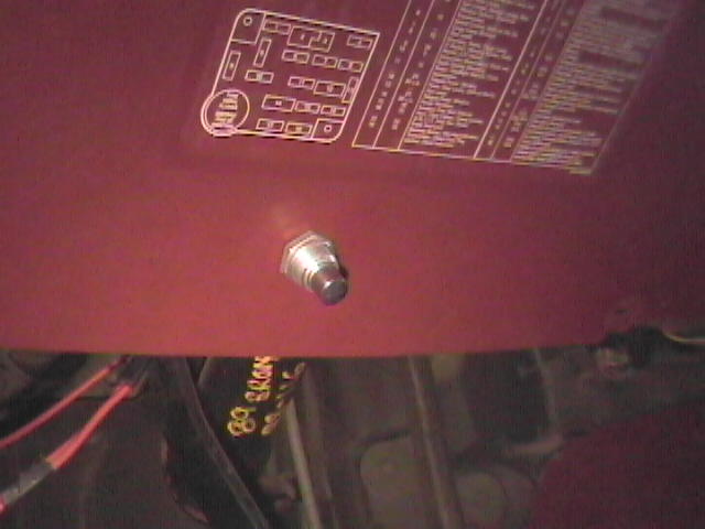 Fuse panel diagram printed on a red interior panel cover with a push-button switch mounted below