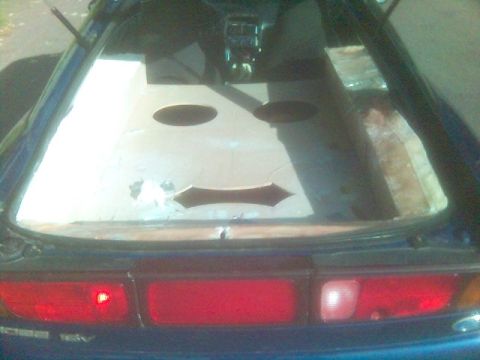 1994 Ford Probe - The rear of a blue car shows a cracked window with a smiley face design cut into it.