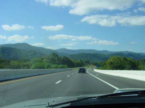 1986 Ford Mustang - Driving on a highway with mountains in the background under a blue sky with clouds.
