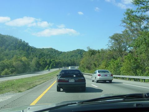 1986 Ford Mustang - A black 1987 Ford Mustang is seen driving on a highway, with another car ahead.
