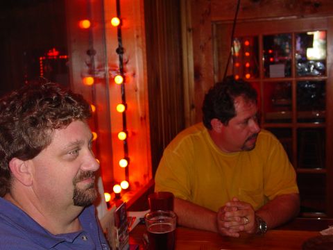 1986 Ford Mustang - Two men are seated at a table in a dimly lit establishment, with decorative orange lights in the background.