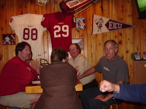 1986 Ford Mustang - A group of men and women are gathered around a table in a room adorned with sports memorabilia.