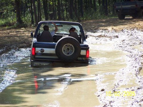 1987 Ford Bronco - Two people are in a 1987 Ford Bronco navigating a muddy path. A second vehicle is in the background.