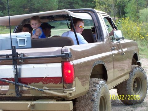 1987 Ford Bronco - Mud-covered Ford Bronco with a lifted suspension and off-road tires is driven by a young man with sunglasses.