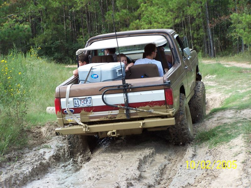 1987 Ford Bronco driving through mud with people in the back