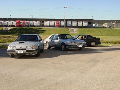 1986 Ford Mustang - Three 1986 Ford Mustangs are parked in front of a warehouse, with FedEx trucks visible in the background.