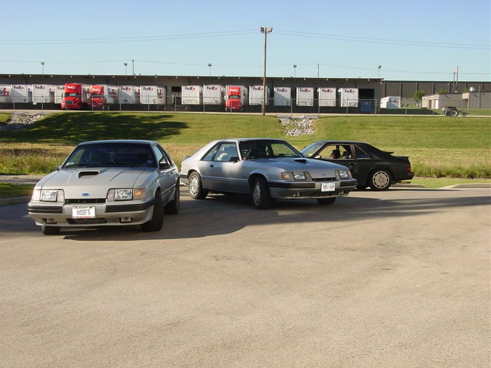 Three 1986 Ford Mustangs parked in front of a warehouse