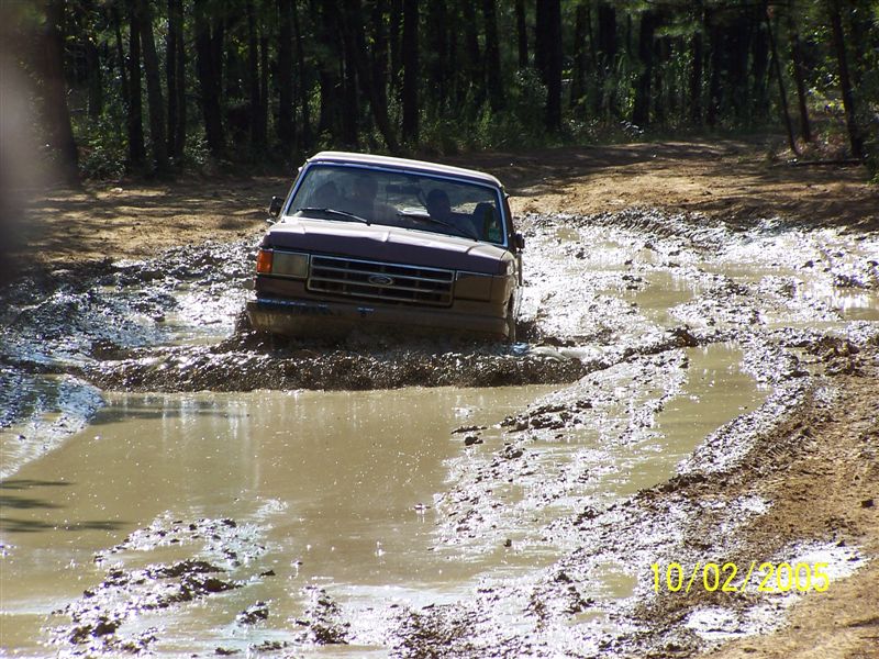 Ford truck stuck in mud on a dirt road, trees in background. Date stamp 10/02/2005