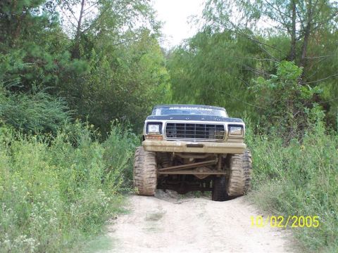 1987 Ford Bronco - A lifted black Ford truck drives on a dirt path surrounded by greenery.