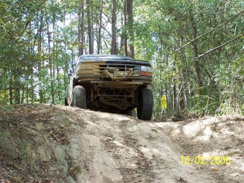 1987 Ford Bronco - Mud-covered 1992 Ford Bronco navigates an off-road trail in a wooded area.