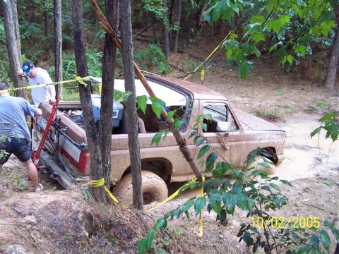 1987 Ford Bronco - A muddy 1980s Ford Bronco is stuck in a ditch while two people attempt to free it.