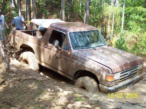 1987 Ford Bronco - A muddy 1987 Ford Bronco is stuck in a ditch with two people nearby.