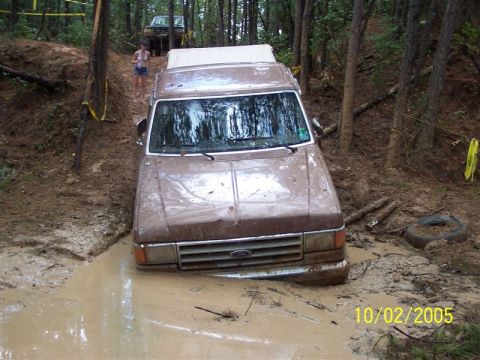 1987 Ford Bronco - A brown Ford Bronco navigates a muddy trail, with another vehicle in the background.