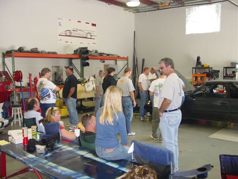 1986 Ford Mustang - A dark 1986 Ford Mustang coupe is parked with its hood open, surrounded by people in a garage setting.