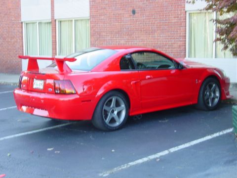 1986 Ford Mustang - A red Ford Mustang with a prominent rear spoiler is parked in a lot.