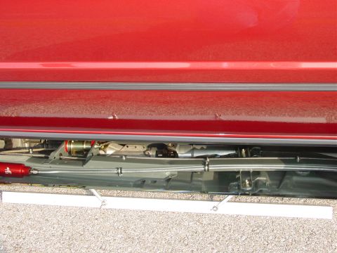 1986 Ford Mustang - Close-up view of a red vehicle's side panel and undercarriage, aftermarket modifications.