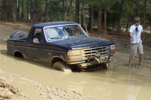 1987 Ford Bronco - Ford Bronco stuck in mud, likely a 1990s model, with a person attempting to pull it out.