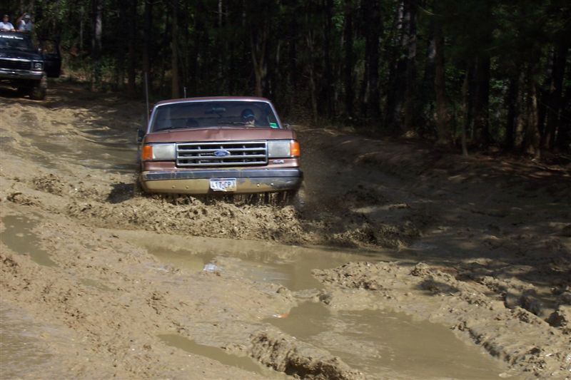 Brown Ford truck driving through a muddy trail, another black SUV is behind it