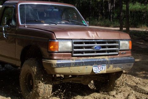 1987 Ford Bronco - A muddy 1987 Ford Bronco navigates off-road terrain.