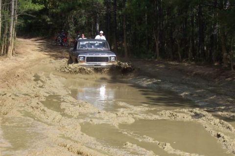 1987 Ford Bronco - A Ford F-Series truck navigates a muddy trail, with "DEEP RESCUE TEAM" visible on its windshield. Other vehicles are visible in the backgro…