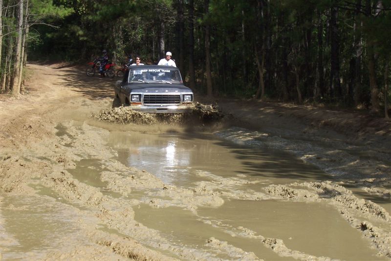 Gray Ford F-Series truck splashing through mud puddle; "DEEP RESCUE TEAM" visible on windshield