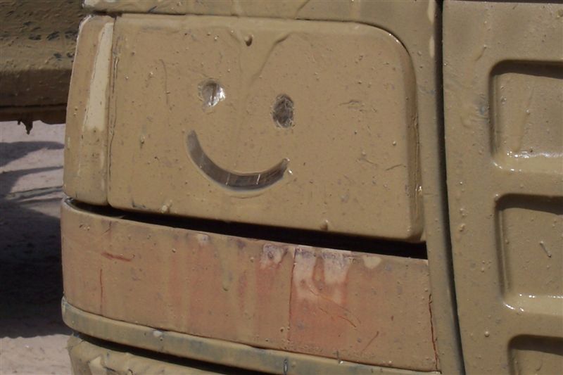 Muddy headlight with a smiley face drawn on it. Part of a vehicle is visible
