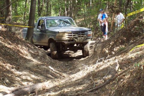 1987 Ford Bronco - This dark-colored truck navigates a challenging muddy incline during an off-road event.