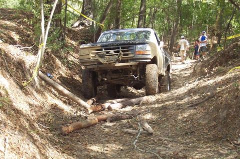 1987 Ford Bronco - Ford Bronco tackles a challenging off-road course with logs and mud on the path.