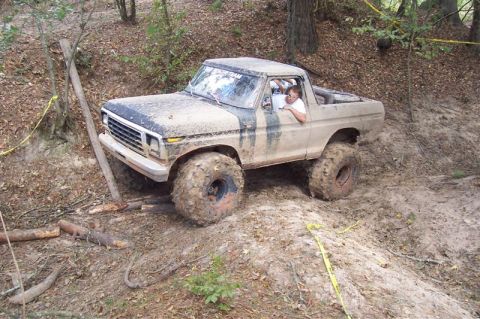 1987 Ford Bronco - A heavily modified 1978 Ford Bronco navigates a muddy, wooded terrain.