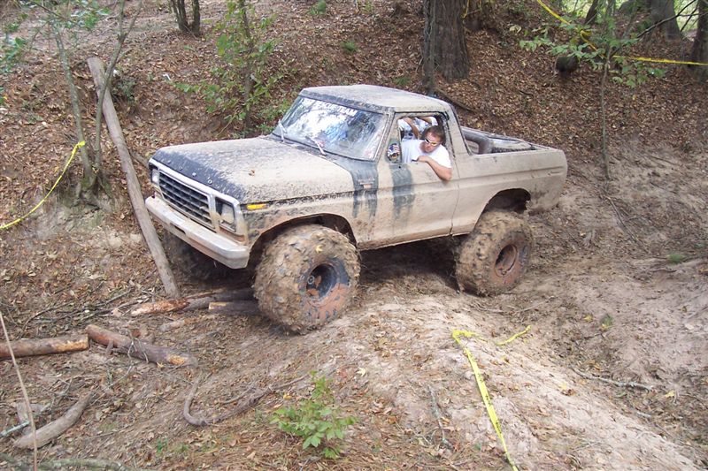 Mud-covered 1978 Ford Bronco with oversized tires driving off-road