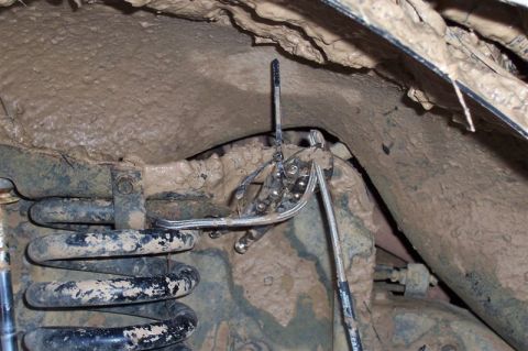 1987 Ford Bronco - Close-up view of heavily soiled suspension parts, showing a coil spring and metal linkages.
