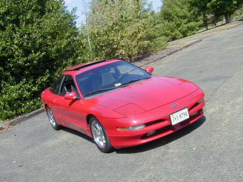 1997 Ford Probe - A red 1997 Ford Probe is parked on a road with trees lining the side.