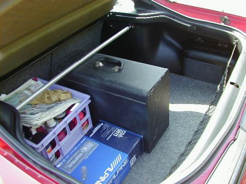 1997 Ford Probe - The trunk of a red car contains a toolbox, a crate with newspapers and cans, and a box for an Alpine car stereo.